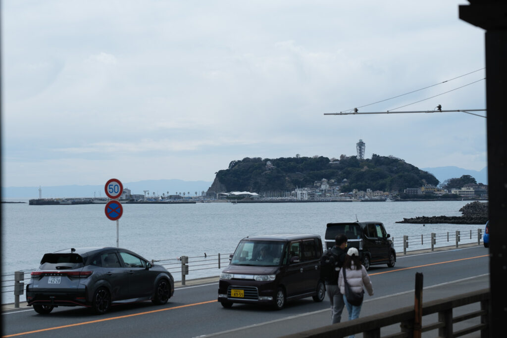 江ノ電の車窓から見た、海沿いの道路の先に浮かぶ江の島