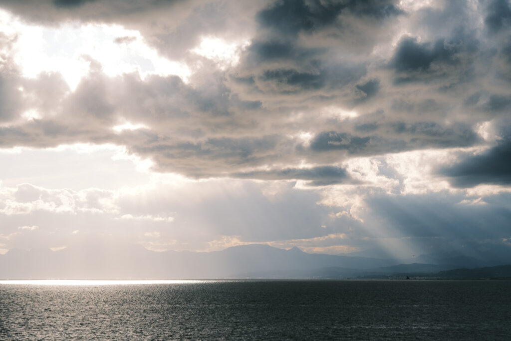 雲の切れ間から海に光が差し込む稚児ヶ淵からの眺め